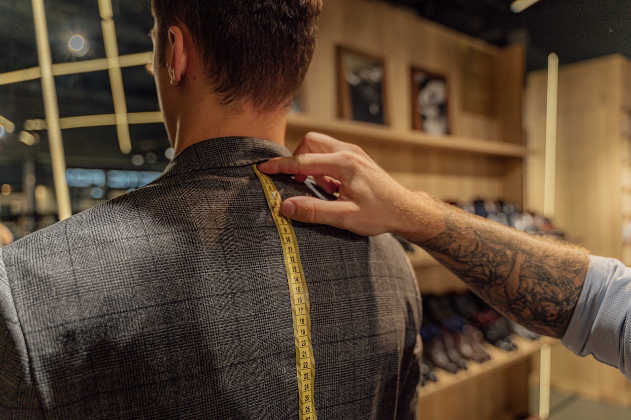 A tailor measuring a client's back with a tape inside a clothing store for a bespoke suit fitting.